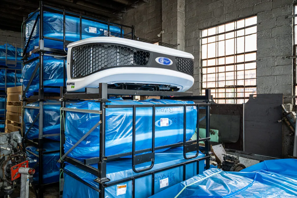 A rustic, industrial garage stacked with brand new, blue-wrapped Carrier branded refrigeration units.